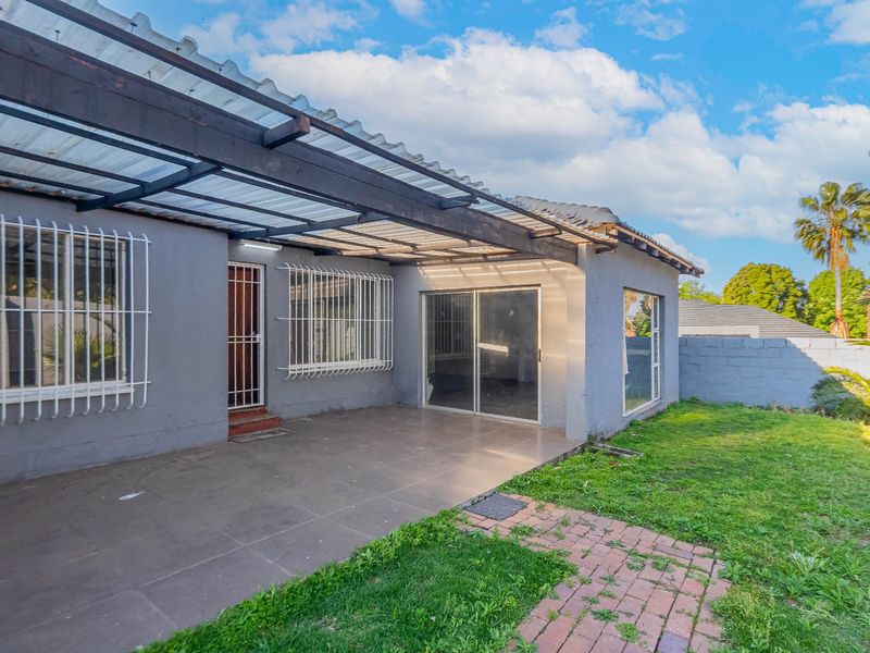 Rear exterior view featuring a covered patio area with sliding glass doors, security bars, and a paved walkway leading to the garden.