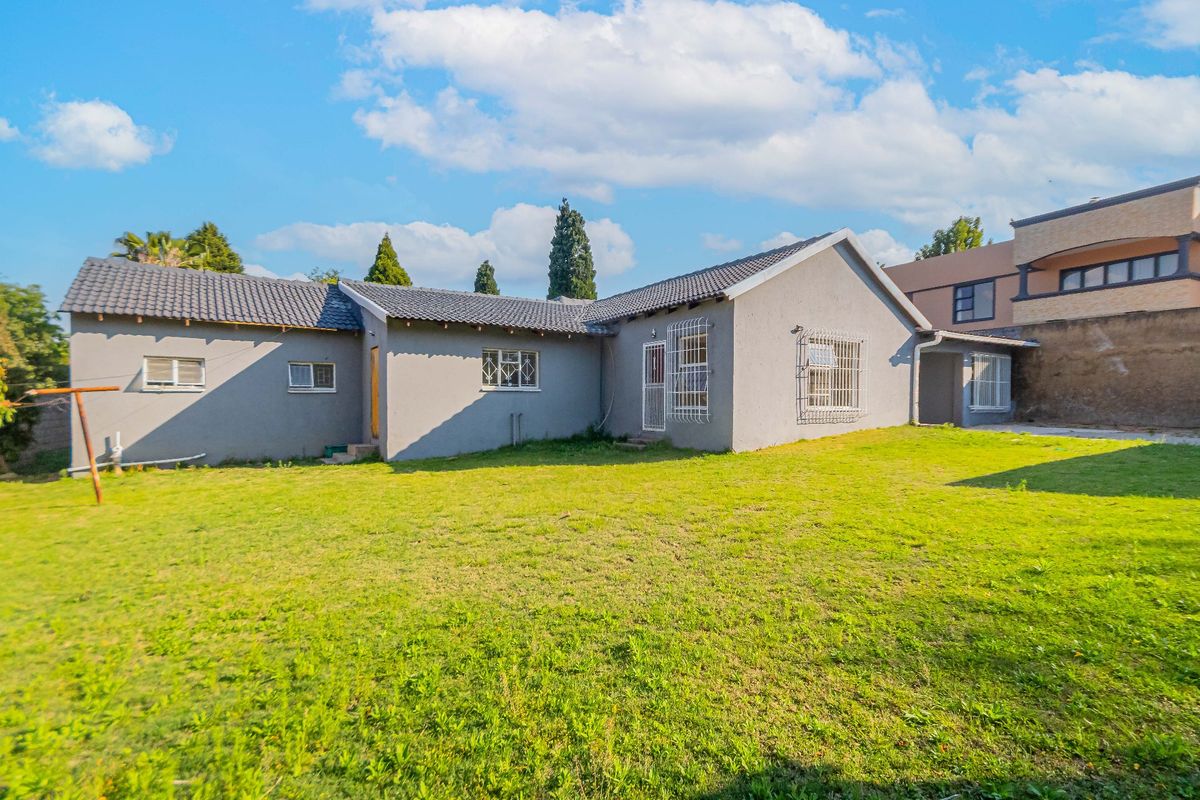 Rear view of the property featuring a spacious lawn, plastered exterior walls, and a tiled roof with security bars on windows.