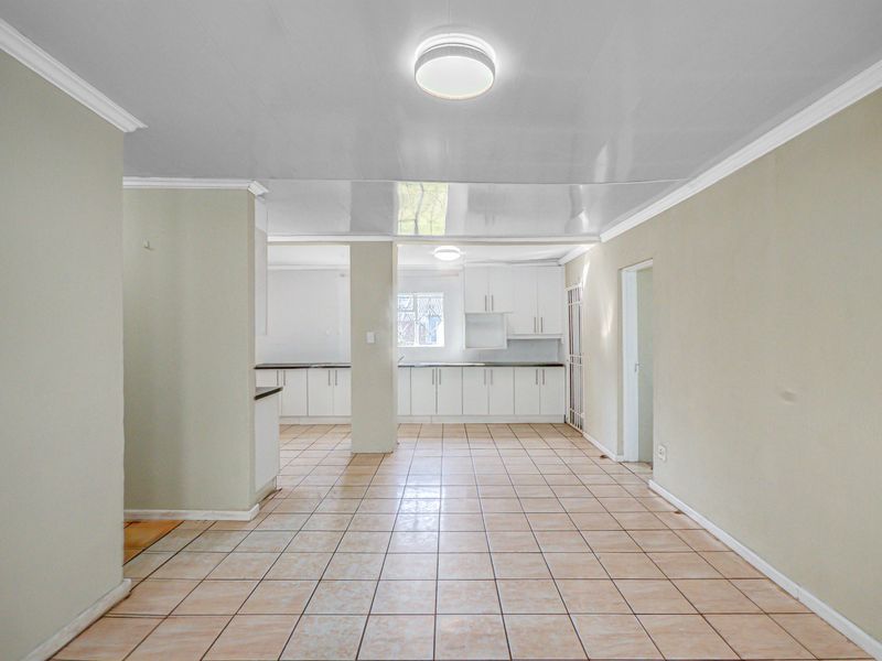 An open-plan living and kitchen area featuring tiled flooring, neutral walls, and built-in white cabinetry, offering a blank canvas for personalization.