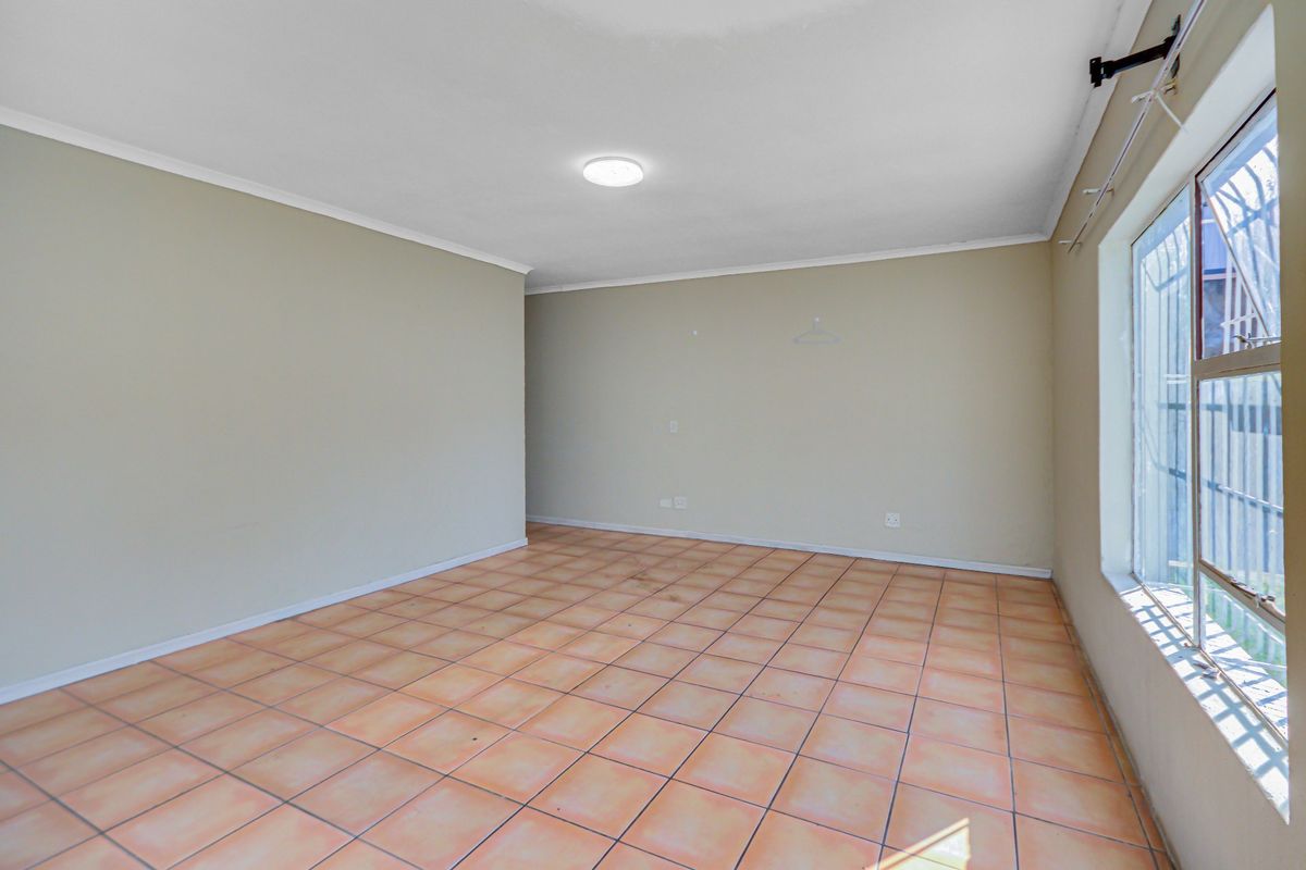 A vacant bedroom featuring neutral wall paint, tiled flooring, and a window fitted with security bars.