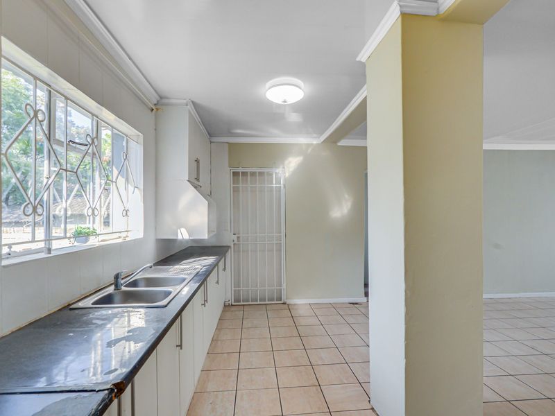 A functional kitchen area featuring tiled flooring, built-in cabinetry, a double sink, and a security gate leading to the exterior.