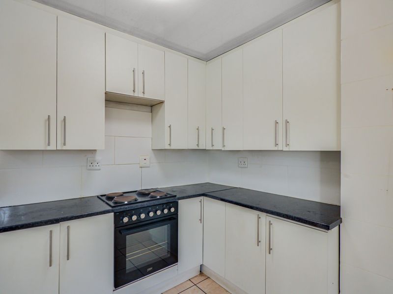 A functional kitchen featuring white built-in cabinetry, dark laminate countertops, and a built-in electric oven and hob with tiled backsplash.