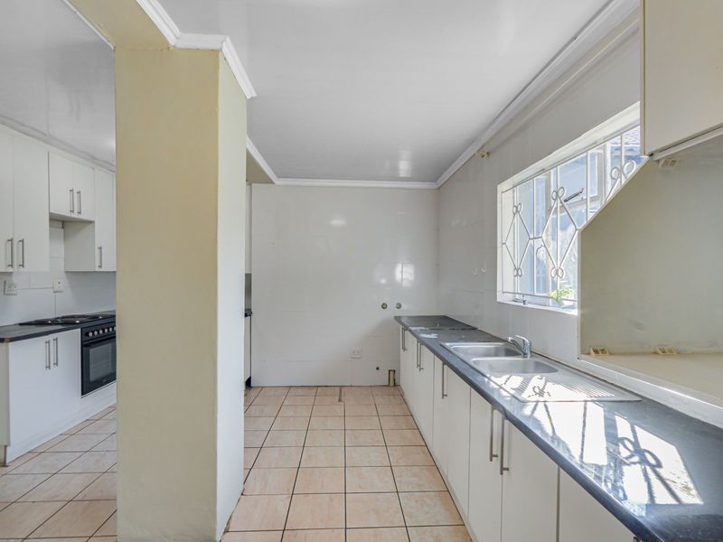 A functional kitchen featuring white cabinetry, dark laminate countertops, built-in oven and hob, and tiled flooring with a window overlooking the exterior.