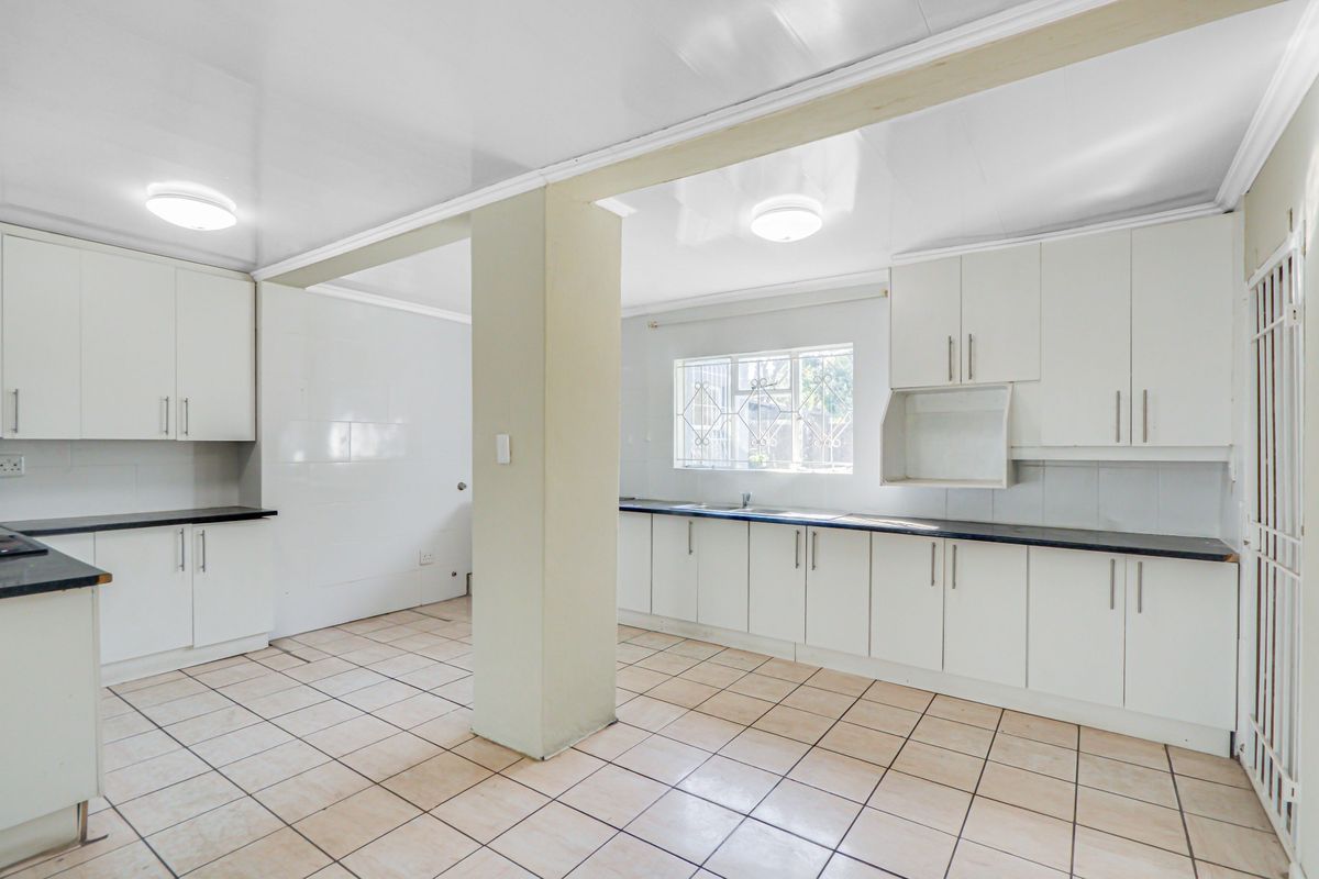 A spacious, empty kitchen featuring white built-in cabinetry, dark laminate countertops, tiled flooring, and a central structural pillar.