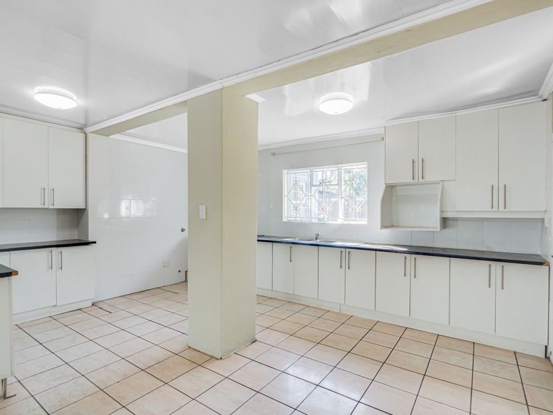 A spacious, empty kitchen featuring white built-in cabinetry, dark laminate countertops, tiled flooring, and a central structural pillar.