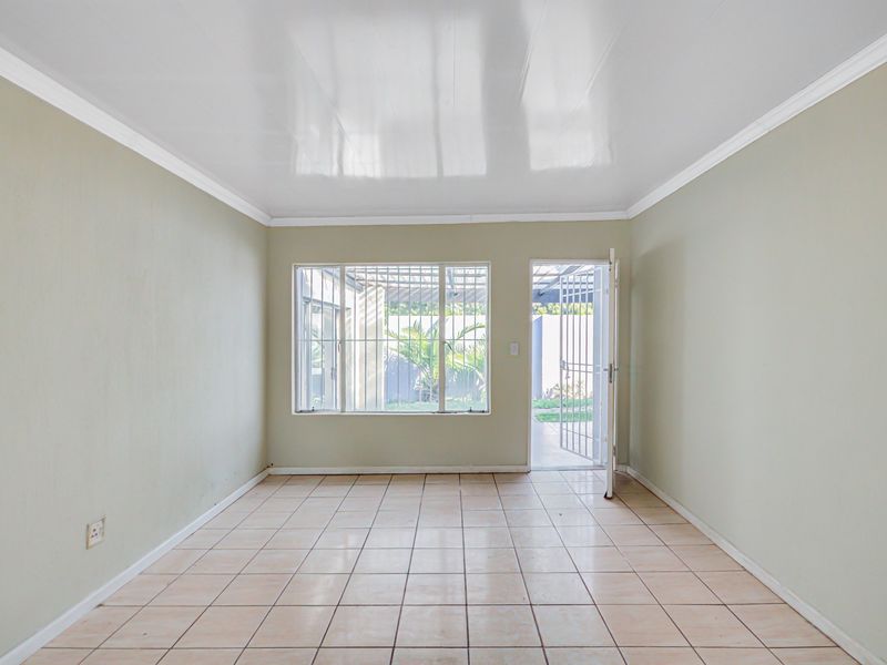An empty living room featuring tiled flooring, a coved ceiling, and direct access to the rear garden through a security gate.