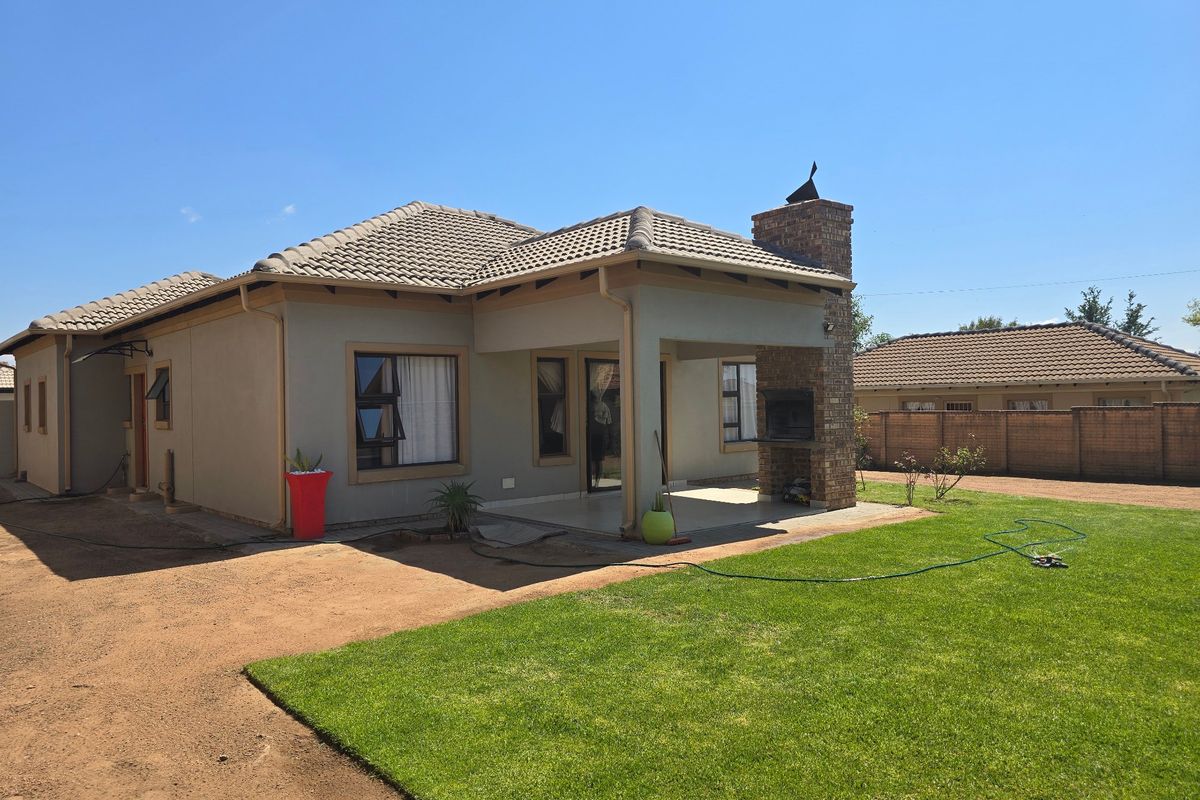 Rear view of the house featuring a covered patio with a built-in brick braai, tiled roof, and a well-maintained lawn.