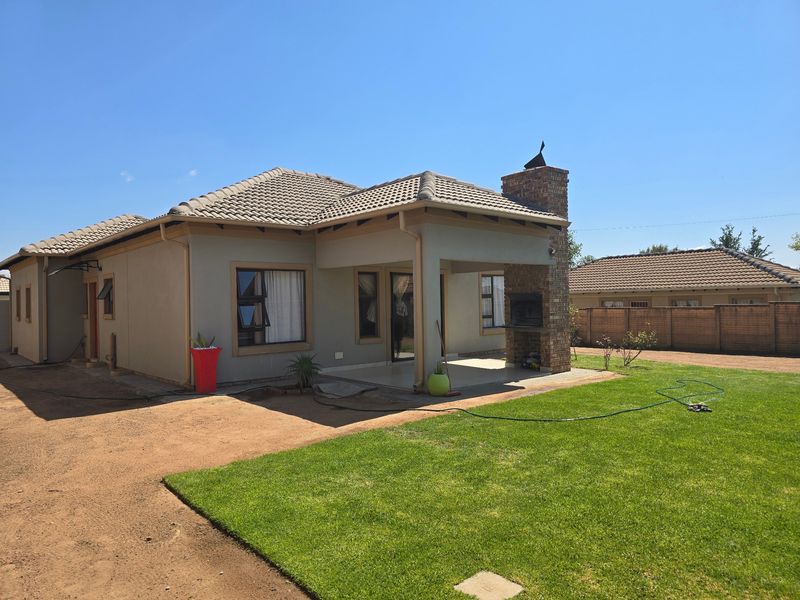 Rear view of the house featuring a covered patio with a built-in brick braai, tiled roof, and a well-maintained lawn.