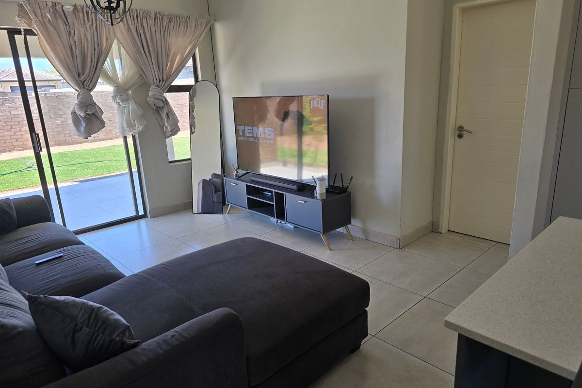A bright living room featuring large sliding glass doors that provide access to the outdoor patio and garden area, complemented by neutral tiled flooring.
