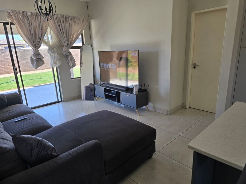A bright living room featuring large sliding glass doors that provide access to the outdoor patio and garden area, complemented by neutral tiled flooring.