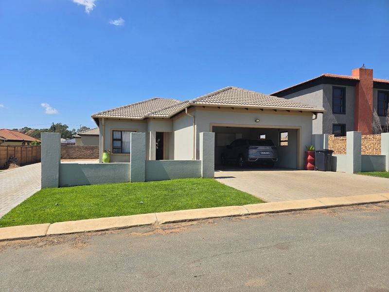 Front view of a modern single-story house featuring a tiled roof, double garage, paved driveway, and a well-maintained front lawn with boundary wall.