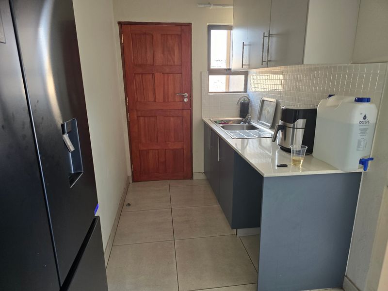 A functional scullery area featuring modern grey cabinetry, stone countertops, a stainless steel sink, and tiled flooring with a timber door.