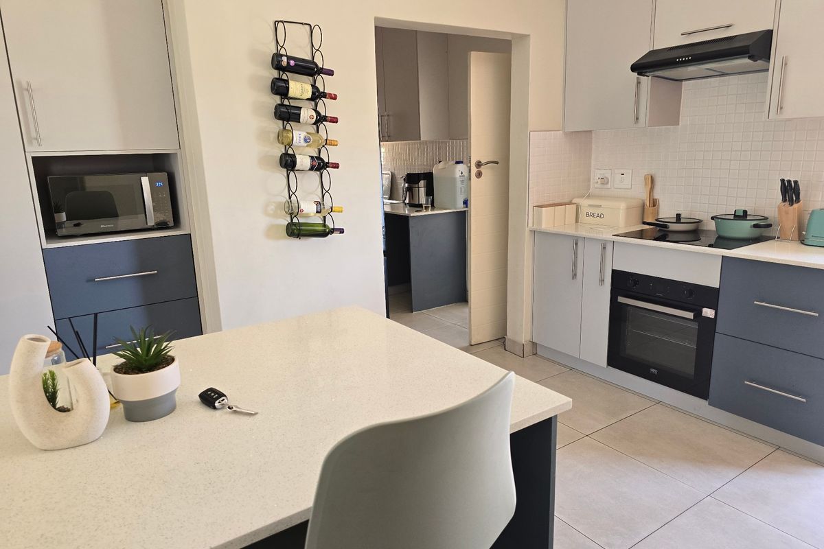 Modern kitchen featuring two-tone cabinetry, stone countertops, integrated appliances, and a tiled backsplash, with an adjacent scullery area visible through the doorway.