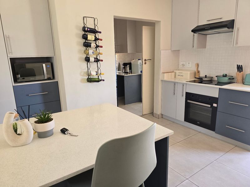 Modern kitchen featuring two-tone cabinetry, stone countertops, integrated appliances, and a tiled backsplash, with an adjacent scullery area visible through the doorway.