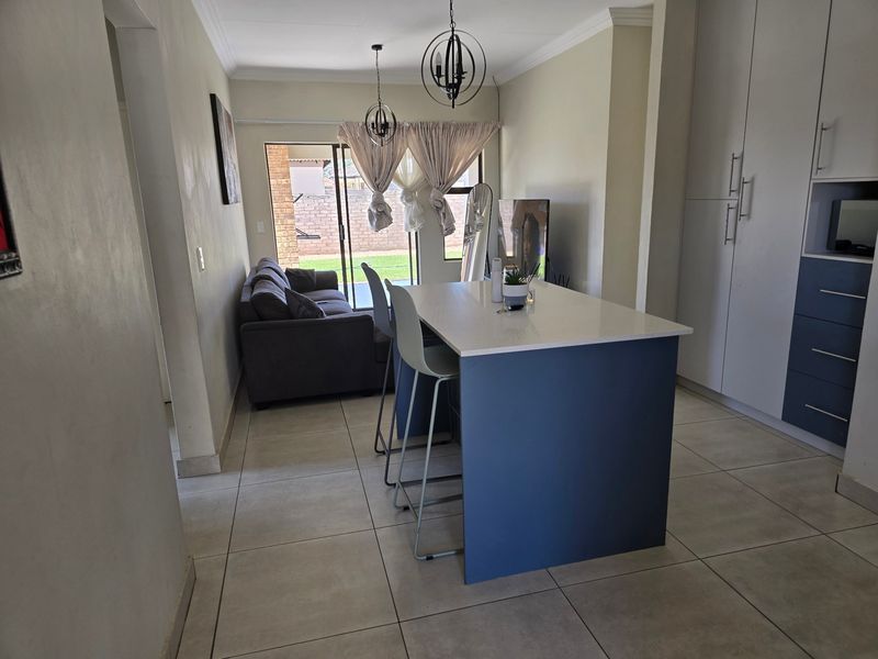 Open-plan living and kitchen area featuring a central island, modern cabinetry, tiled flooring, and direct access to the rear garden through sliding glass doors.