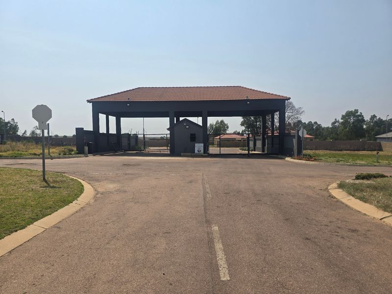 A view of the residential estate entrance featuring a covered security gatehouse and paved access road.