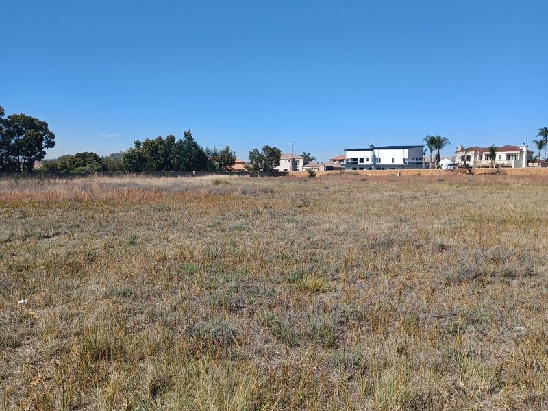 A wide-angle view of a vacant residential plot featuring dry grass and a perimeter boundary wall in the background.