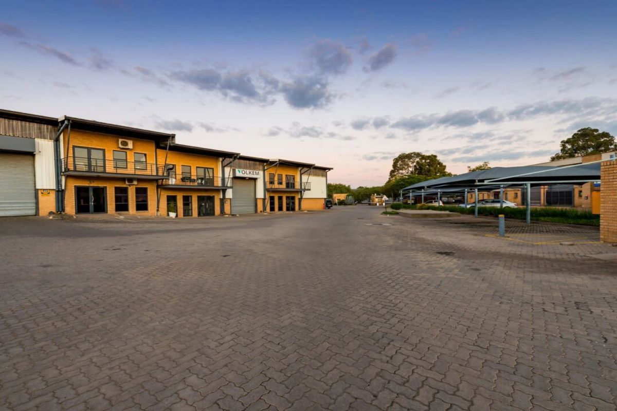 Exterior view of an industrial complex featuring roller shutter doors, paved yard space, and covered parking bays.