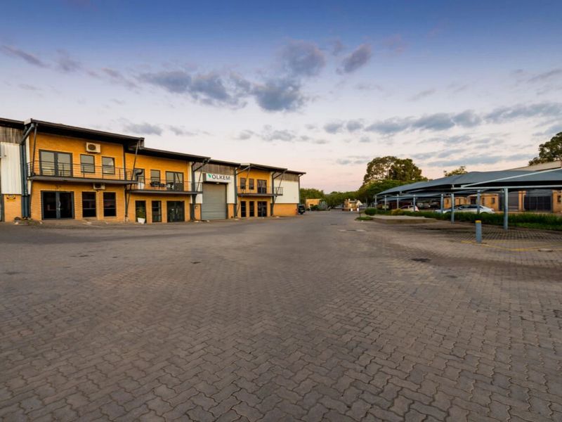 Exterior view of an industrial complex featuring roller shutter doors, paved yard space, and covered parking bays.
