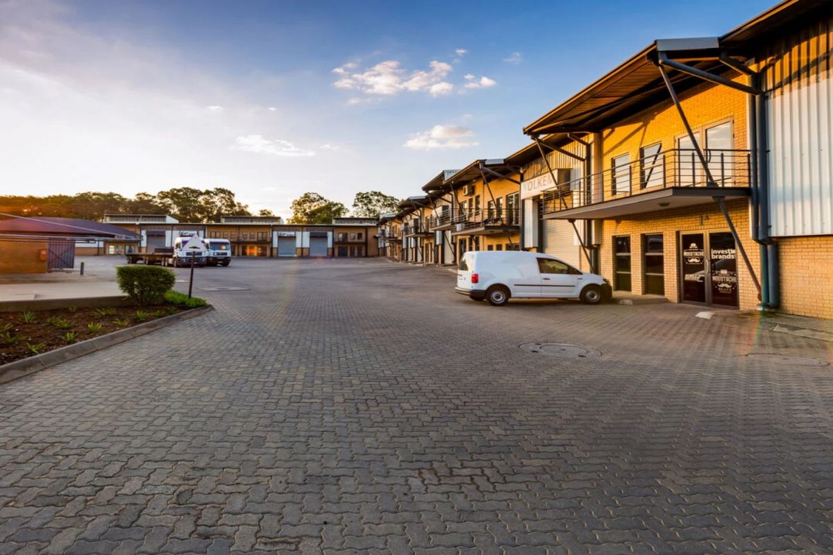 A wide-angle view of an industrial business park featuring paved driveway access, multi-level units with balconies, and functional roller shutter doors.