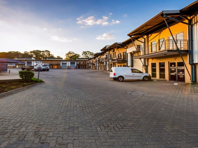 A wide-angle view of an industrial business park featuring paved driveway access, multi-level units with balconies, and functional roller shutter doors.