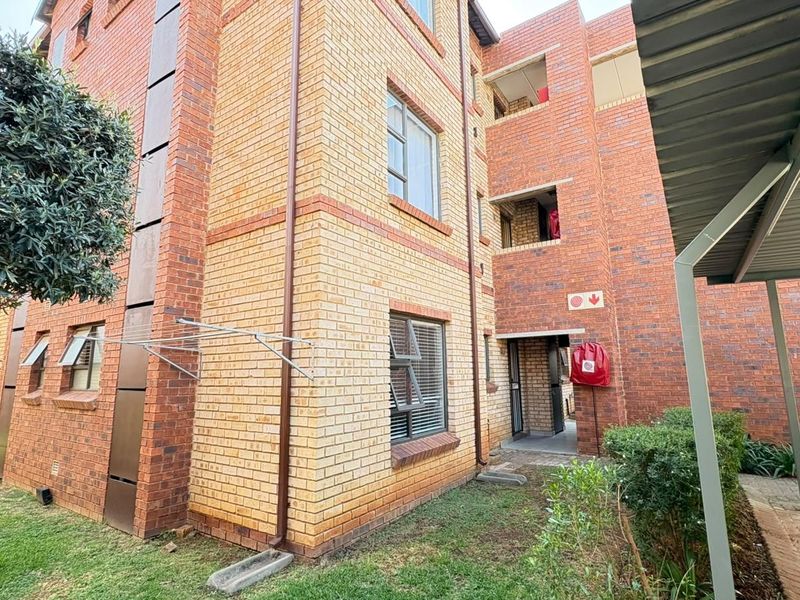 Exterior view of a multi-story face brick apartment building featuring paved walkways, aluminium window frames, and a covered carport area.