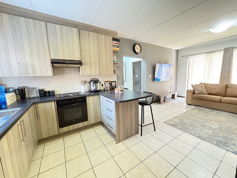 Open-plan living area featuring a modern kitchen with light wood cabinetry, laminate countertops, built-in oven and hob, and tiled flooring throughout.