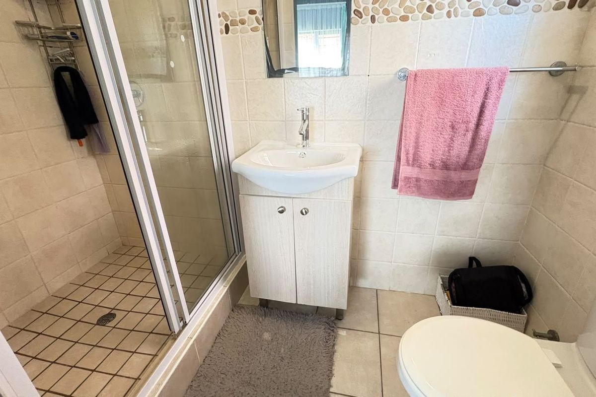 A functional bathroom featuring a shower enclosure, vanity unit with basin, and toilet, finished with neutral wall and floor tiling.