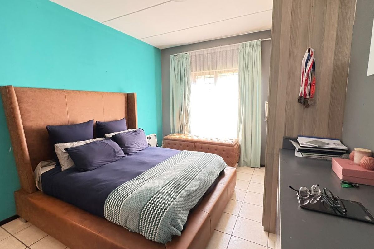 A bedroom featuring tiled flooring and a built-in wardrobe, with a bright window and a vibrant accent wall.