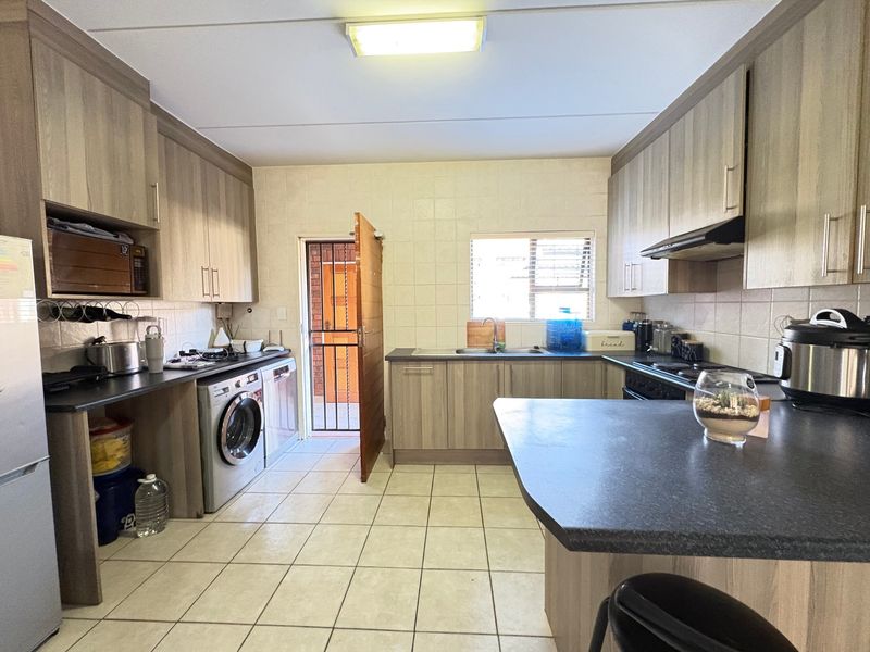 Functional kitchen featuring laminate cabinetry, dark countertops, tiled flooring, and integrated appliances with direct access to an exterior area.