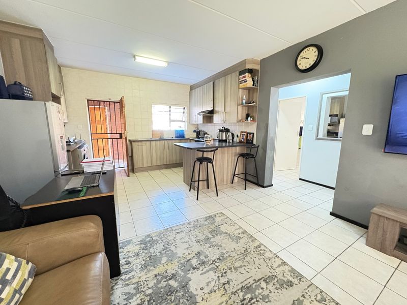Open-plan living and kitchen area featuring tiled flooring, built-in cabinetry, a kitchen island, and a security gate leading to the exterior.