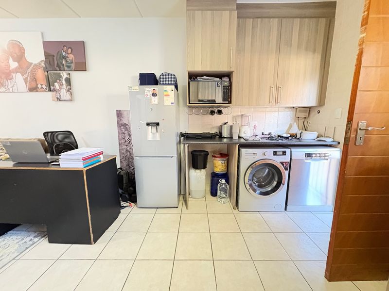 A functional kitchen area featuring built-in cabinetry, tiled flooring, and integrated laundry and dishwasher appliances.