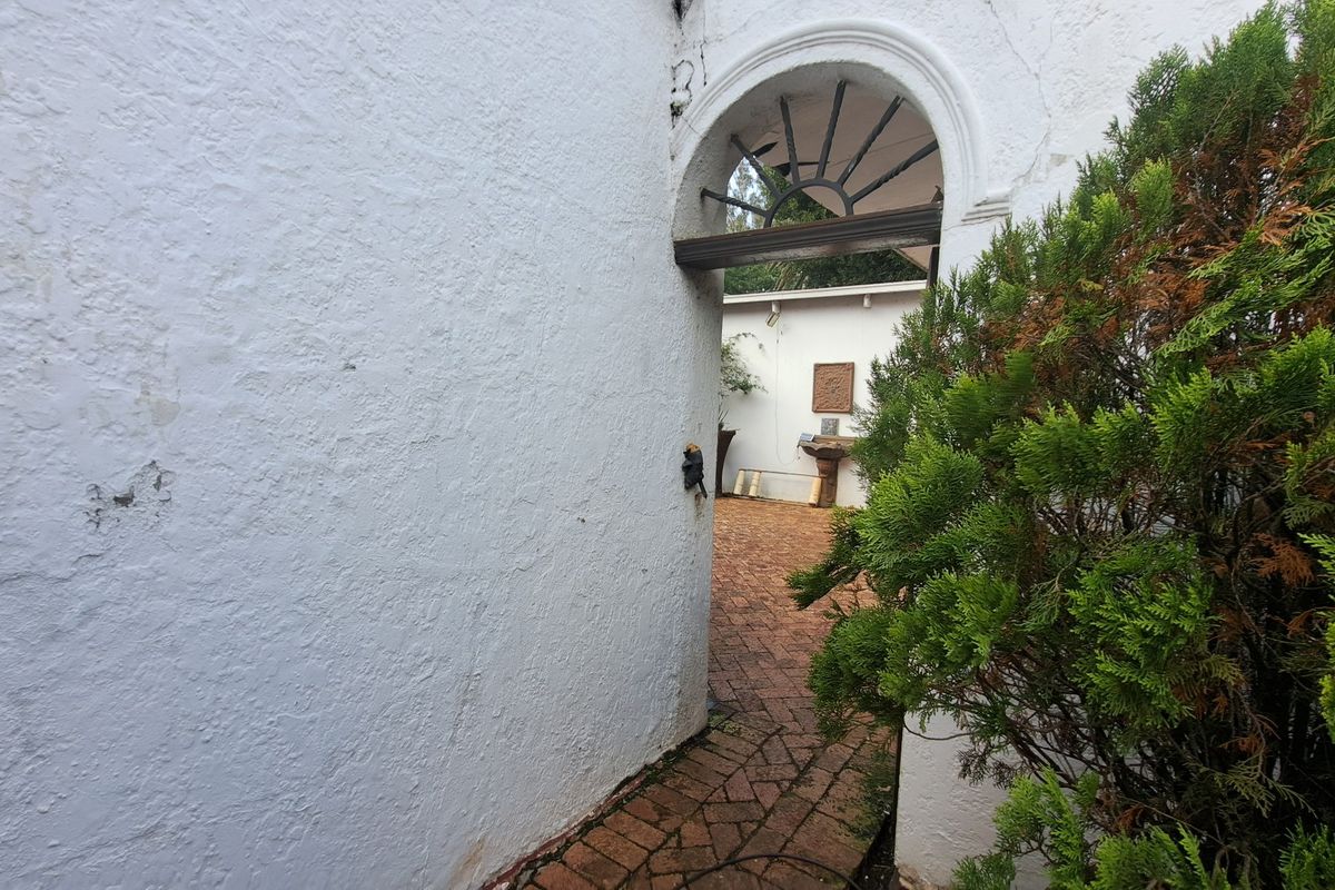 A view through an arched masonry doorway leading to a brick-paved rear courtyard area with weathered finishes.