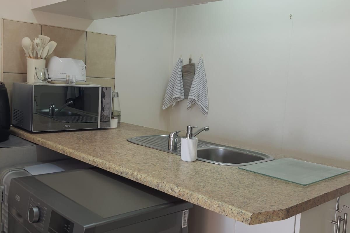 A functional kitchen area featuring laminate countertops, a stainless steel sink with mixer tap, and built-in cabinetry with tiled splashback.