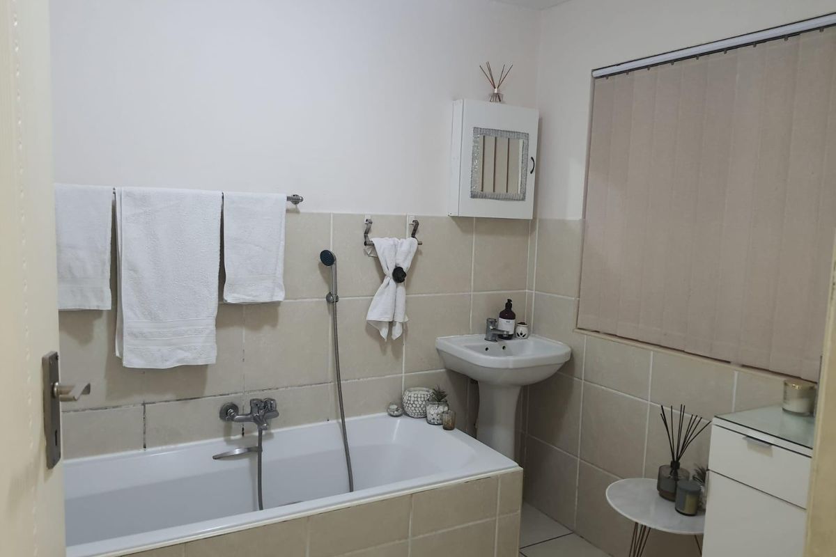 A functional bathroom featuring a built-in bathtub, pedestal basin, and neutral wall tiling, providing a clean and practical space.