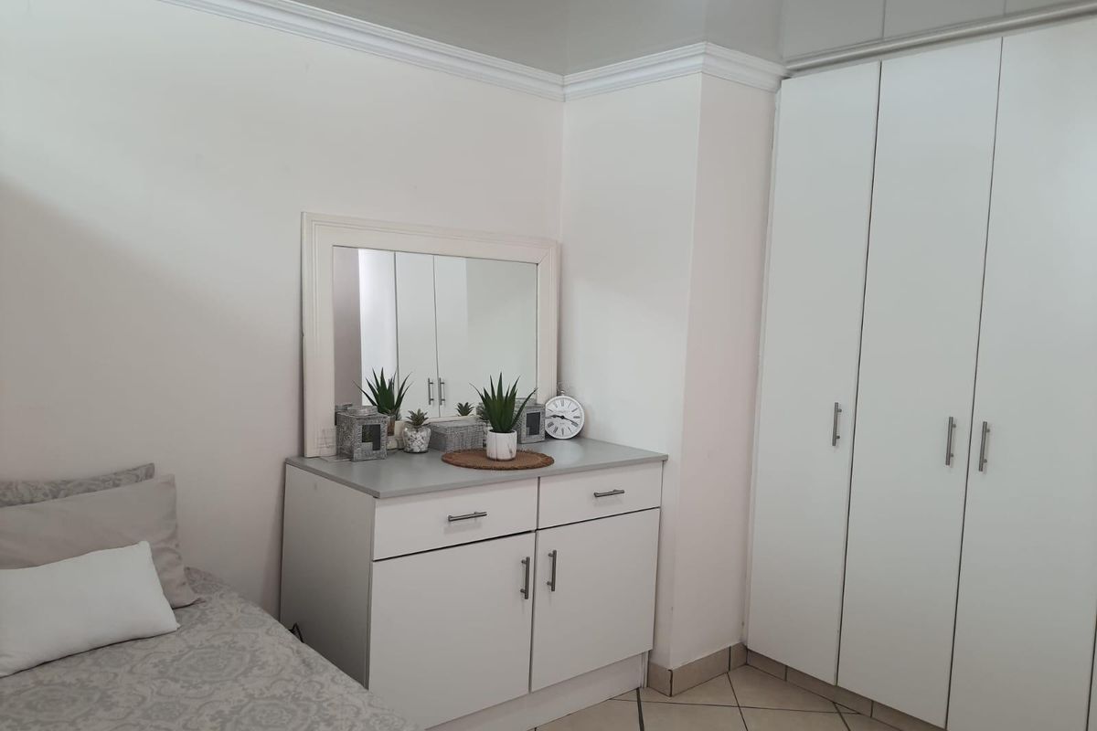 A bedroom featuring neutral tiled flooring, white built-in cupboards, and decorative crown molding, providing a clean and functional living space.