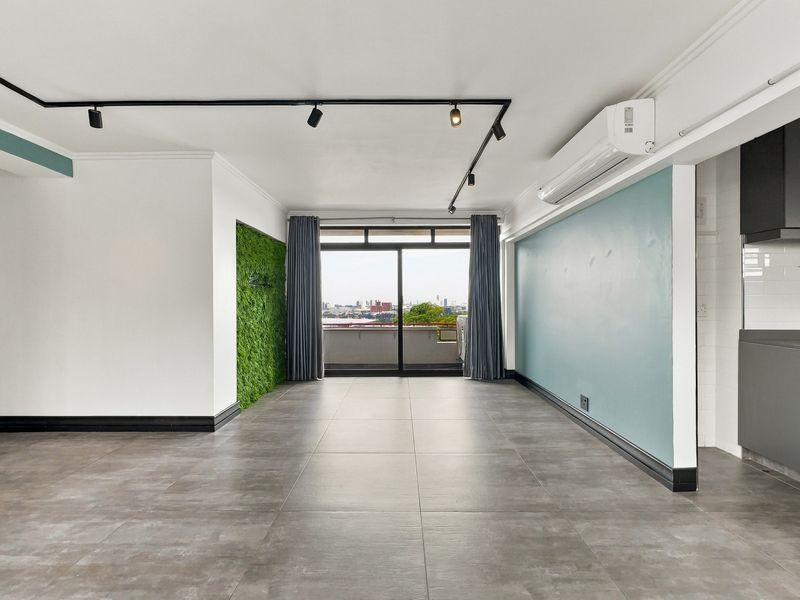 Spacious open-plan living area featuring modern tiled floors, track lighting, split-system air conditioning, and direct access to a balcony with city views.