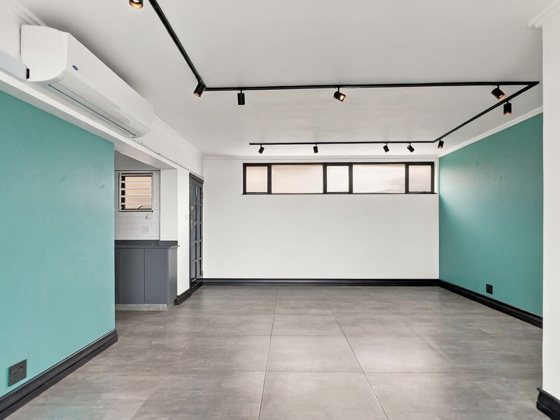 A bright, open-plan living area featuring modern grey floor tiles, track lighting, and a wall-mounted split-system air conditioner.