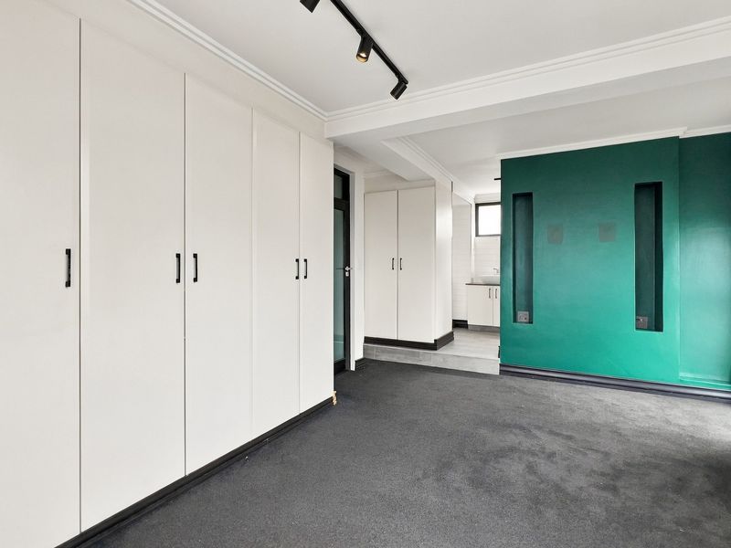 Spacious bedroom featuring extensive built-in cupboards, modern track lighting, and a striking green feature wall with recessed shelving niches.