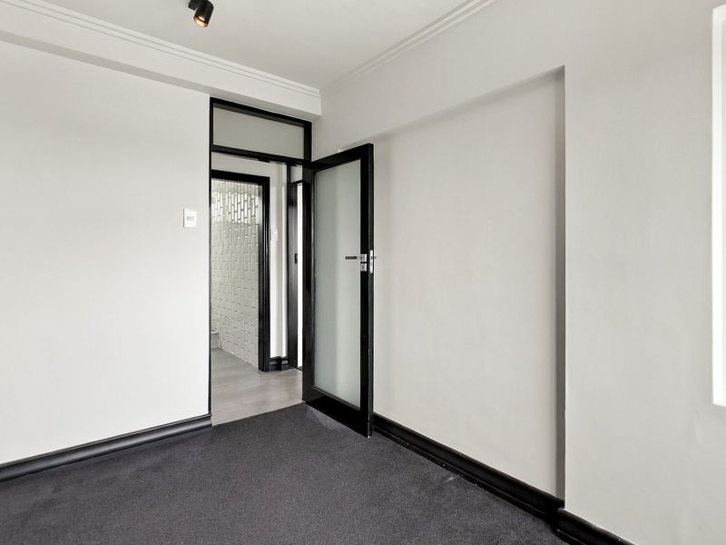 A clean, modern hallway featuring dark carpet, contrasting black door frames, and a frosted glass door leading to an adjacent tiled space.