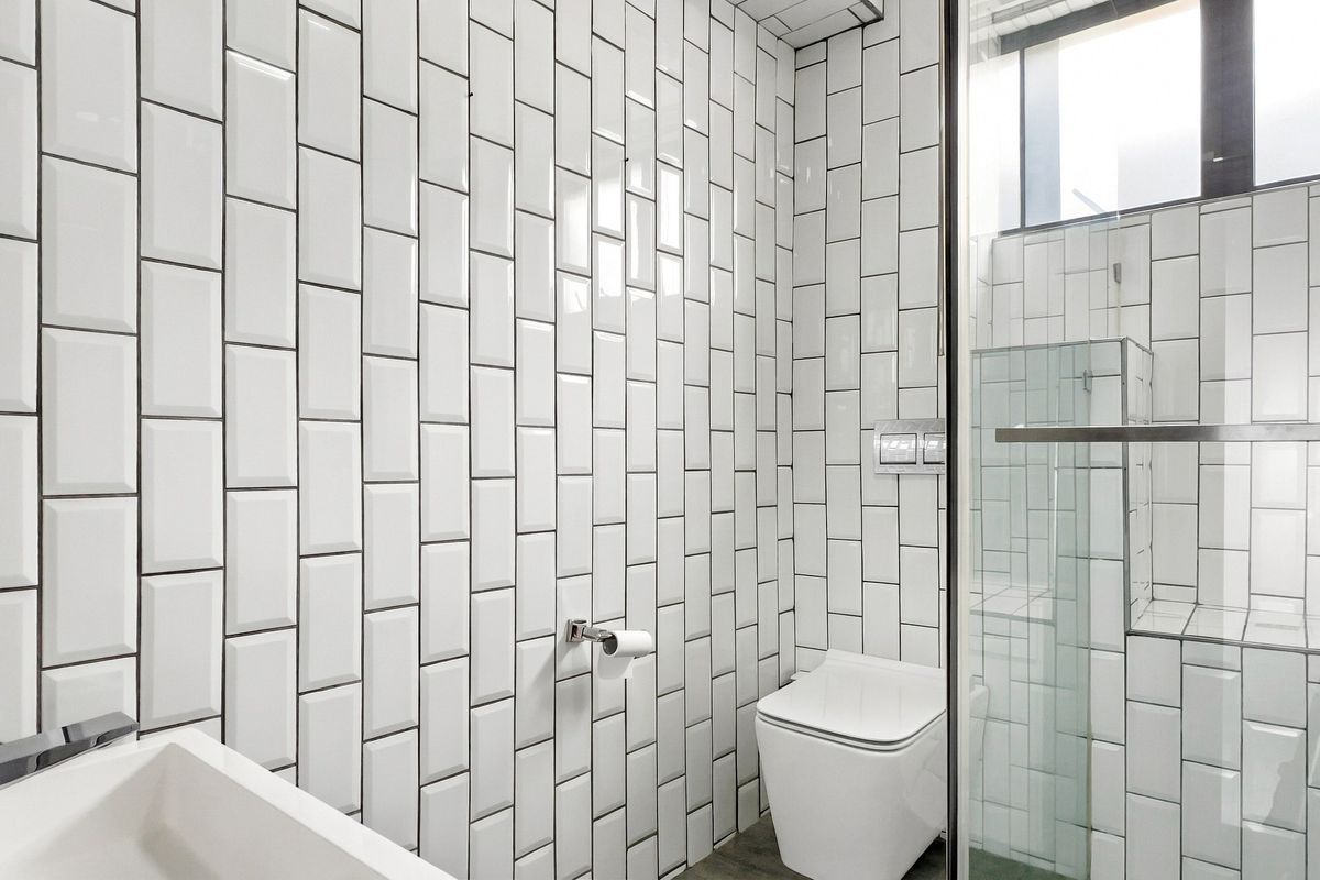 Modern bathroom featuring white subway wall tiles, a wall-mounted toilet with integrated flush plate, and a glass-enclosed shower area.