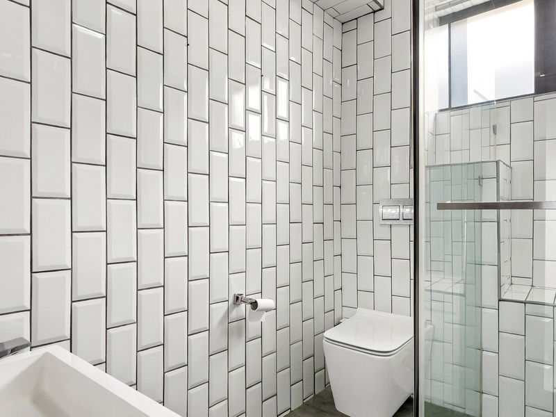 Modern bathroom featuring white subway wall tiles, a wall-mounted toilet with integrated flush plate, and a glass-enclosed shower area.