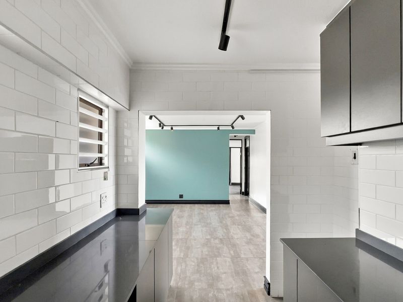 Modern kitchen featuring sleek dark cabinetry, stone countertops, and white subway tile backsplash, leading into an open-plan living area with contemporary track lighting.