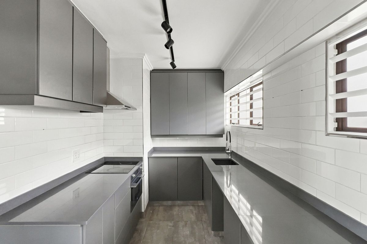 Modern galley kitchen featuring sleek grey cabinetry, stone countertops, subway tile backsplash, and integrated appliances with contemporary track lighting.