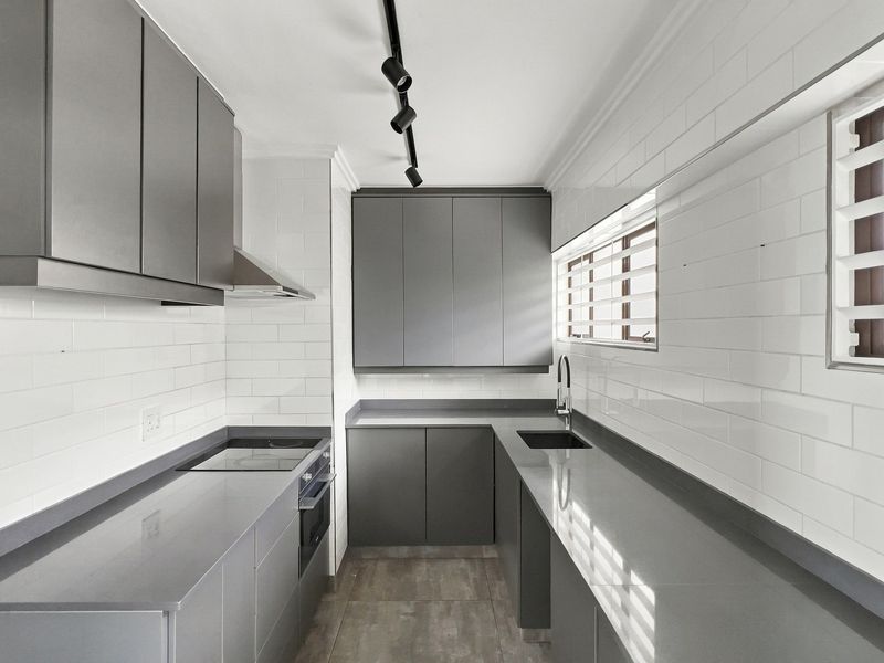 Modern galley kitchen featuring sleek grey cabinetry, stone countertops, subway tile backsplash, and integrated appliances with contemporary track lighting.