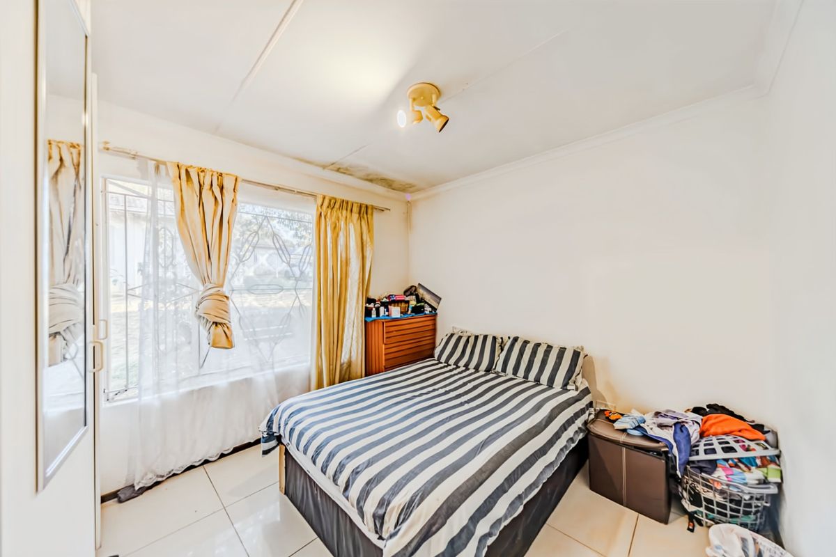 A bedroom featuring tiled flooring, a large wall-mounted mirror, and security bars on the window, with visible water staining on the ceiling.