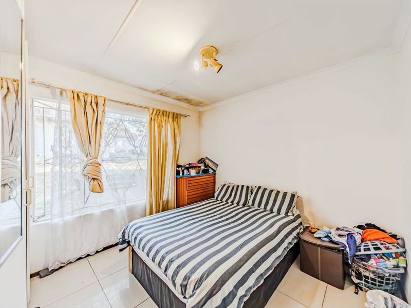 A bedroom featuring tiled flooring, a large wall-mounted mirror, and security bars on the window, with visible water staining on the ceiling.
