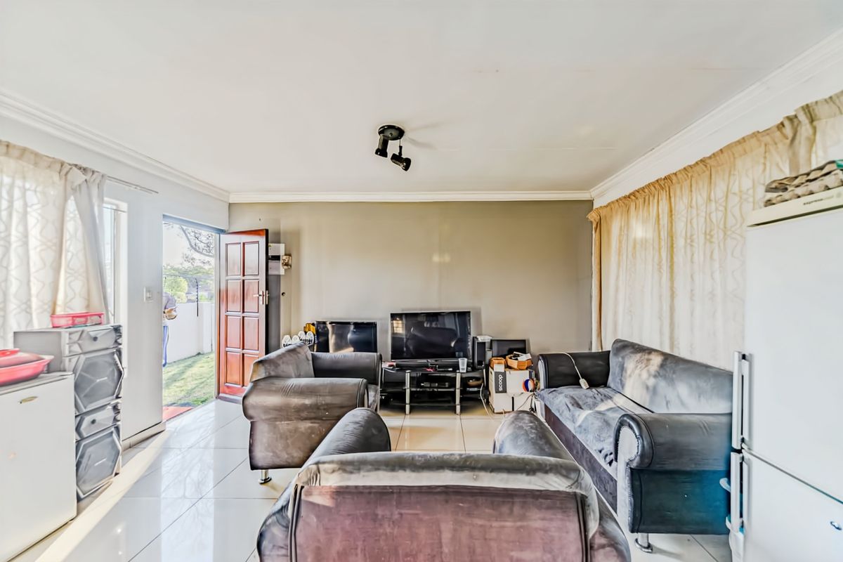 A living room featuring tiled flooring, ceiling spotlighting, and direct access to the exterior through a timber door.