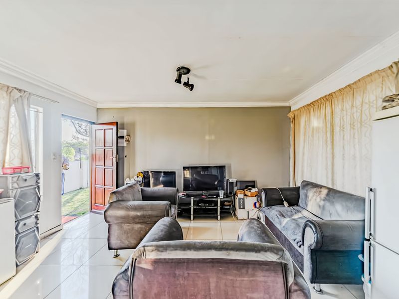 A living room featuring tiled flooring, ceiling spotlighting, and direct access to the exterior through a timber door.