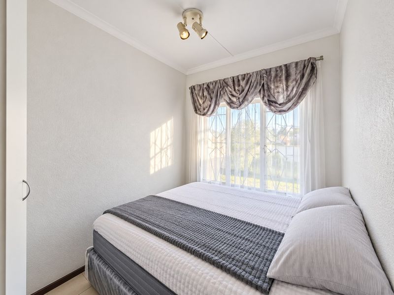 A well-lit bedroom featuring built-in storage, security bars on the window, and neutral finishes, providing a comfortable and functional living space.
